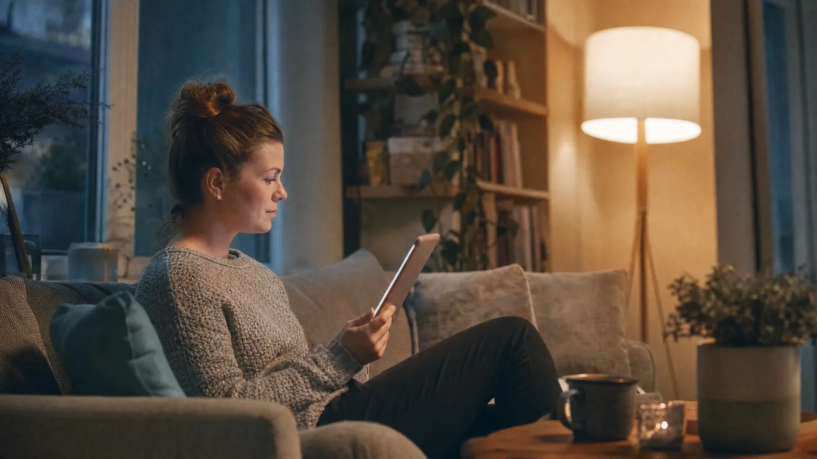 Person sitzt abends auf dem Sofa und liest auf dem Tablet