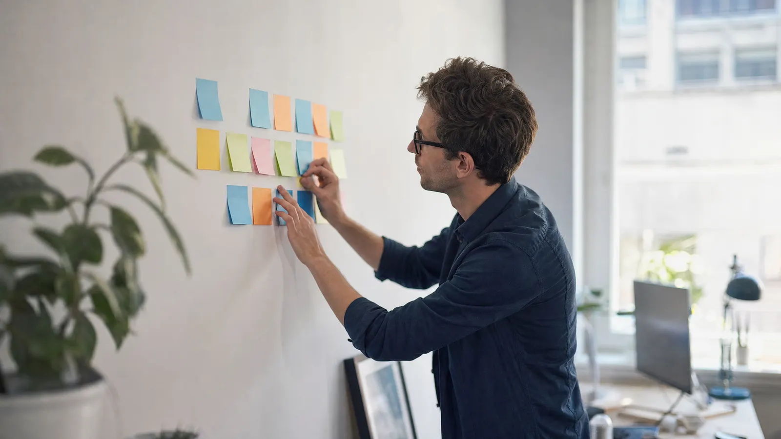 Person ordnet Haftnotizen an einer Wand