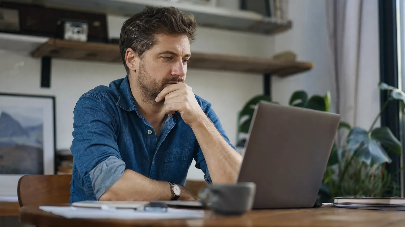 Person sitzt nachdenklich vor dem Laptop, die Hand am Kinn